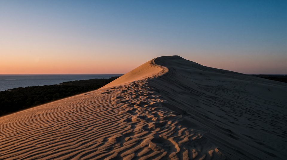 Crête d'une grande dune de sable au crépuscule, lumière rasante et ombres longues, ciel sans nuage